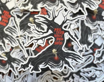 Pode incluir: Adesivo preto e branco com uma árvore estilizada e o texto vermelho "You reap what you sow". O design da árvore inclui uma caveira e uma chave. Vários adesivos são visíveis.