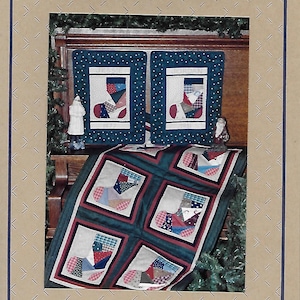 May include: A quilt pattern featuring a patchwork design of red, white, and blue stockings. The quilt is displayed on a wooden mantel with two smaller pillows featuring the same design. The pattern is titled "Liberty Homestead".