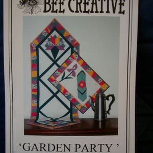 May include: A quilting pattern for a 'Garden Party' table runner, featuring a 3-piece unit design with a floral motif. The pattern is 17 inches by 50 inches and includes a full-size pattern and layout guide. The pattern is by Eunice Hill.