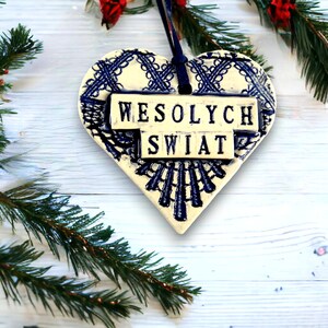 Puede incluir: Adorno de cer&aacute;mica blanca en forma de coraz&oacute;n con dise&ntilde;o de encaje azul y las palabras "Wesołych Świąt" en letras negras.