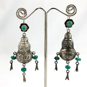 May include: A pair of silver dangle earrings with turquoise stones. The earrings are shaped like gourds and have intricate floral designs.