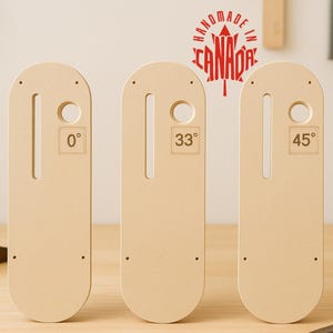 Peut inclure: Trois gabarits d'angle en bois avec des indications de degrés : 0°, 33° et 45°. Chaque outil comporte une fente et un trou circulaire. Le texte "HANDMADE IN CANADA" est imprimé en rouge au-dessus des outils. Les outils sont en bois clair.