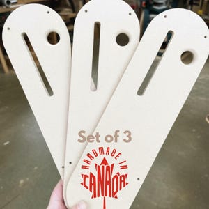 May include: Set of three off-white wooden woodworking jigs. Each jig has a curved top with a hole, a long slot, and two small holes. The text "Set of 3" and "HANDMADE IN CANADA" with a maple leaf logo are printed in red.