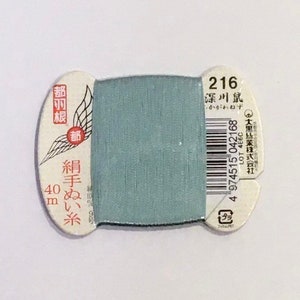 May include: A spool of light blue thread with a white label that says "216 深川鼠" and "絹手ぬい糸 40m".
