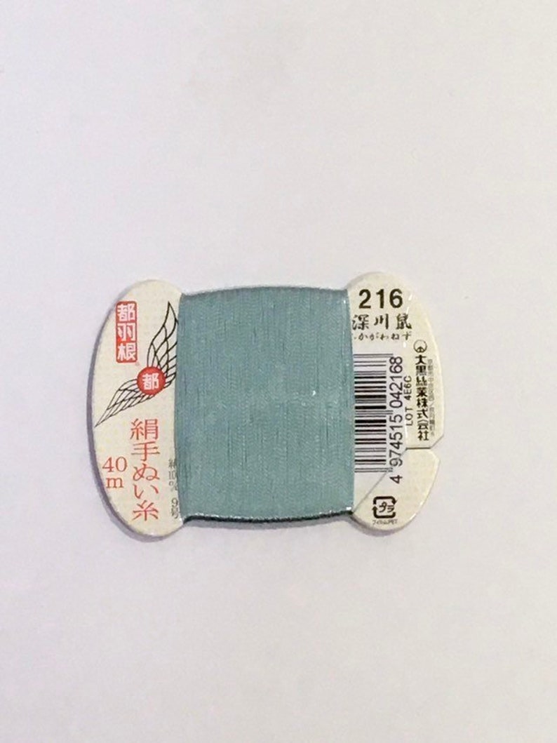 May include: A spool of light blue thread with a white label that says "216 深川鼠" and "絹手ぬい糸 40m".