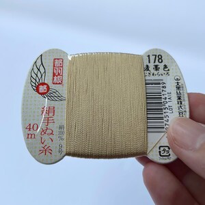 May include: A spool of beige sewing thread with Japanese text and a barcode. The label features a wing design and the number 178. The thread is 40 meters long.