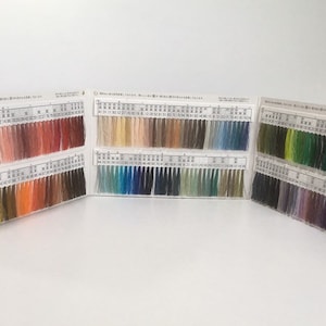May include: A colour chart with rows of thread samples in various colours, including red, orange, yellow, green, blue, purple, and black. The chart is divided into sections with numbers and Japanese text.