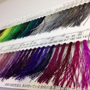 May include: A close-up of a color chart with rows of different colored threads. The chart is labeled with numbers and the text "日本の伝統色名は、糸が付いている台紙の裏面に".