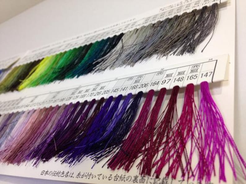 May include: A close-up of a color chart with rows of different colored threads. The chart is labeled with numbers and the text "日本の伝統色名は、糸が付いている台紙の裏面に".
