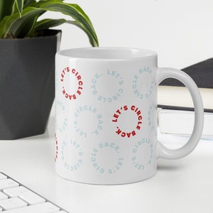 White workplace buzzword coffee mug with text that reads "let's circle back" in pale blue and bright red