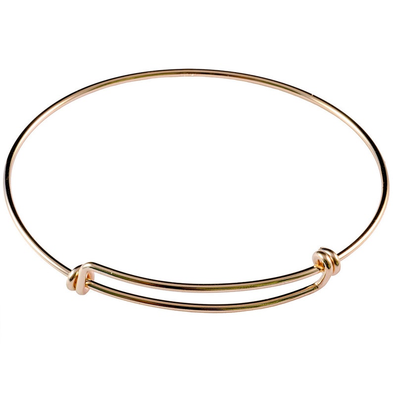 May include: A gold-colored adjustable bangle bracelet. The bracelet features a simple, circular design with a sliding mechanism for size adjustment. The metal has a shiny finish, reflecting light. The bracelet is designed to be worn on the wrist.