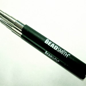 May include: A set of two retractable beading tools with black cases. The tools are made of metal and have the words "The Beadsmith" printed on the cases.