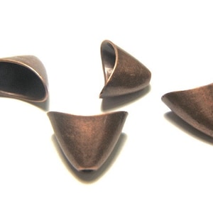 May include: Four copper-colored metal cone-shaped beads with a hollowed-out top. The beads are approximately 1 inch in length.