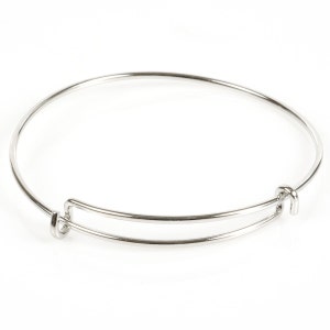 May include: A silver-colored adjustable bangle bracelet. The bracelet has a circular design with a sliding mechanism for size adjustment. The metal has a shiny, reflective surface. The bracelet is shown against a white background.