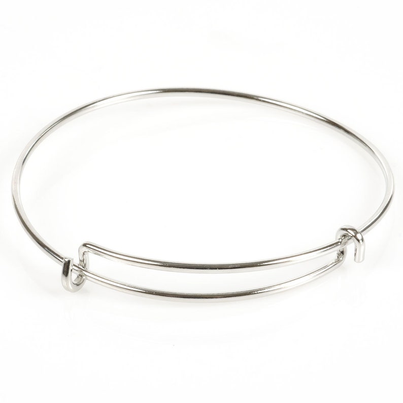 May include: A silver-colored adjustable bangle bracelet. The bracelet has a circular design with a sliding mechanism for size adjustment. The metal has a shiny, reflective surface. The bracelet is shown against a white background.