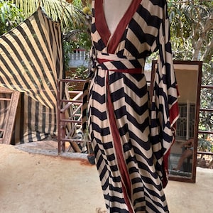 Puede incluir: Un vestido largo de rayas blancas y negras con ribete rojo. El vestido tiene un escote en V y un estilo de envoltura. El vestido est&aacute; hecho de una tela ligera y tiene una silueta fluida.
