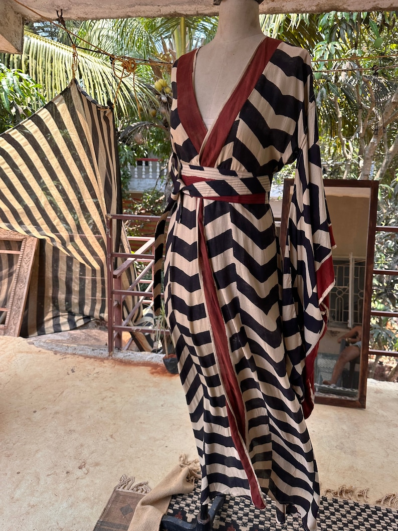 Puede incluir: Un vestido largo de rayas blancas y negras con ribete rojo. El vestido tiene un escote en V y un estilo de envoltura. El vestido est&aacute; hecho de una tela ligera y tiene una silueta fluida.