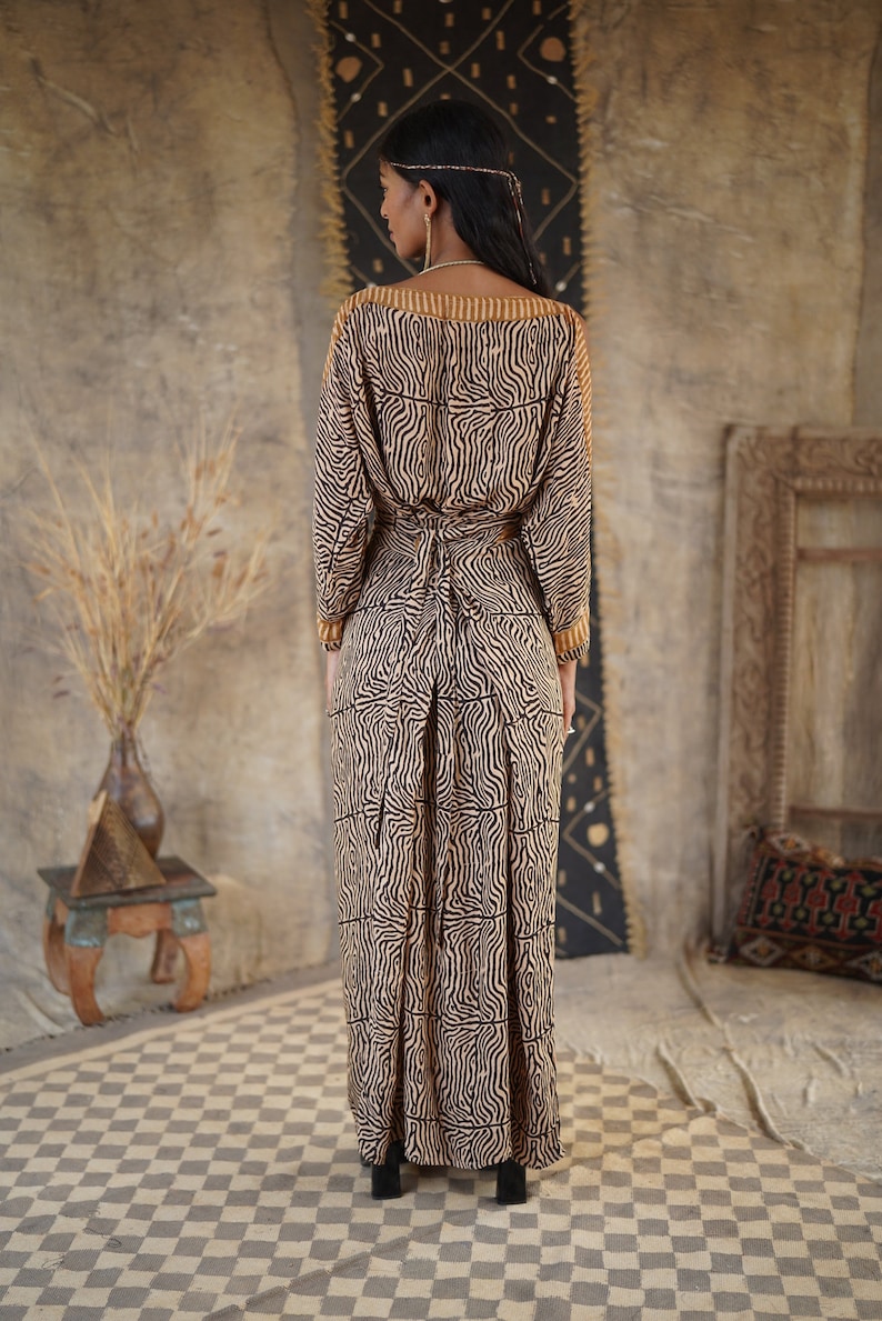 May include: A long, flowing dress with a brown and black zebra print. The dress has a V-neck and long sleeves. The dress is tied at the waist with a brown belt.