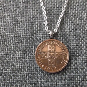 May include: A silver chain necklace with a copper-colored Portuguese coin pendant. The coin features the Portuguese coat of arms and the year 1976.