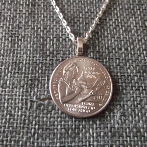 May include: Silver chain necklace with a silver quarter coin pendant featuring a woman's profile and the words "In God We Trust" and "Liberty 1982".
