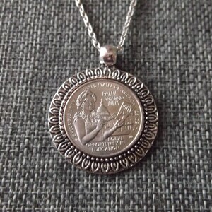 May include: Silver necklace with a pendant featuring a Susan B. Anthony dollar coin. The coin has an image of Susan B. Anthony and the inscription "EQUAL OPPORTUNITY IN EDUCATION".