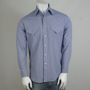 May include: A blue and white checkered long-sleeve shirt with two chest pockets and a button-down collar. The shirt is paired with blue jeans.