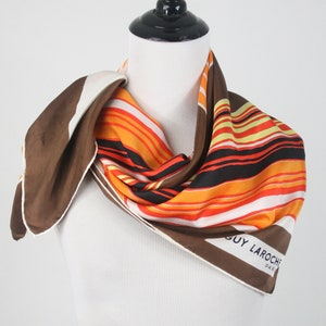 May include: A brown, orange, white, and black striped silk scarf with the words 'GUY LAROCHE PARIS' printed on the bottom right corner.
