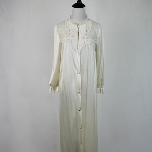 May include: A long, white satin nightgown with a lace collar and pink floral embroidery. The gown has a button-up front and long sleeves.