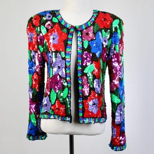 May include: A colorful, sequined jacket with a floral design. The jacket features red, blue, purple, and green sequins arranged in a flower pattern. The jacket is displayed on a mannequin against a white background.