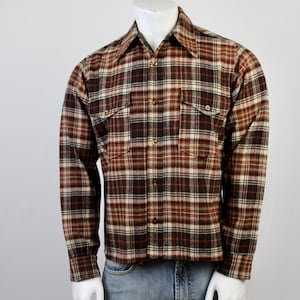 May include: A long-sleeved plaid shirt in shades of brown, red, and cream. The shirt has two chest pockets and button closures. The shirt is paired with blue jeans.