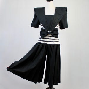 May include: A vintage black and white jumpsuit displayed on a mannequin. The top features a square neckline and short sleeves with a large bow at the waist. The bottom consists of wide-leg pants. The outfit has a nautical theme.