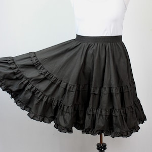May include: A dark gray, tiered skirt with multiple ruffled layers. The skirt has an elastic waistband and is displayed on a mannequin. The skirt is a solid color and appears to be made of a lightweight fabric.