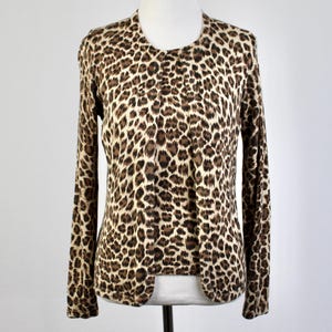 May include: A long-sleeved cardigan with a leopard print pattern. The open-front sweater features a round neckline and is displayed on a mannequin. The animal print consists of brown spots on a beige background.