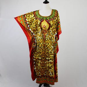 May include: A floor-length kaftan dress featuring a vibrant yellow and black leopard print pattern. The garment includes a round neckline with green and red circular accents, a drawstring waist, and wide sleeves with solid red trim borders.