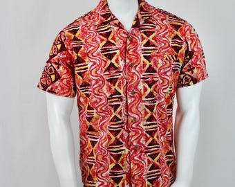 Op de afbeelding: Korte mouwen overhemd met een opvallend geometrisch patroon in rood, geel en zwart. Het overhemd heeft een klassieke kraag en wordt op een mannequin getoond. De outfit wordt gecombineerd met een blauwe jeans.