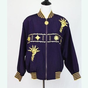 May include: A purple bomber jacket with gold embroidery of suns and stars. The jacket has a zipper closure and ribbed cuffs and waistband.