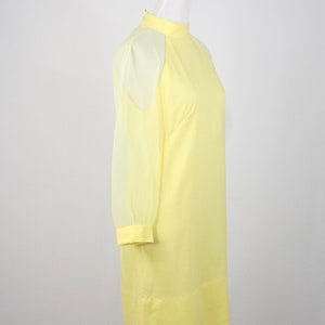 May include: A yellow dress with sheer sleeves. The dress has a high neckline and a simple, straight silhouette.