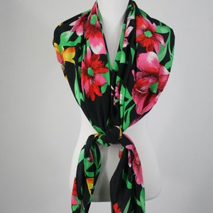 May include: A black silk scarf with a floral print featuring large pink, red, and yellow flowers on a black background. The scarf is tied around a white mannequin's neck.