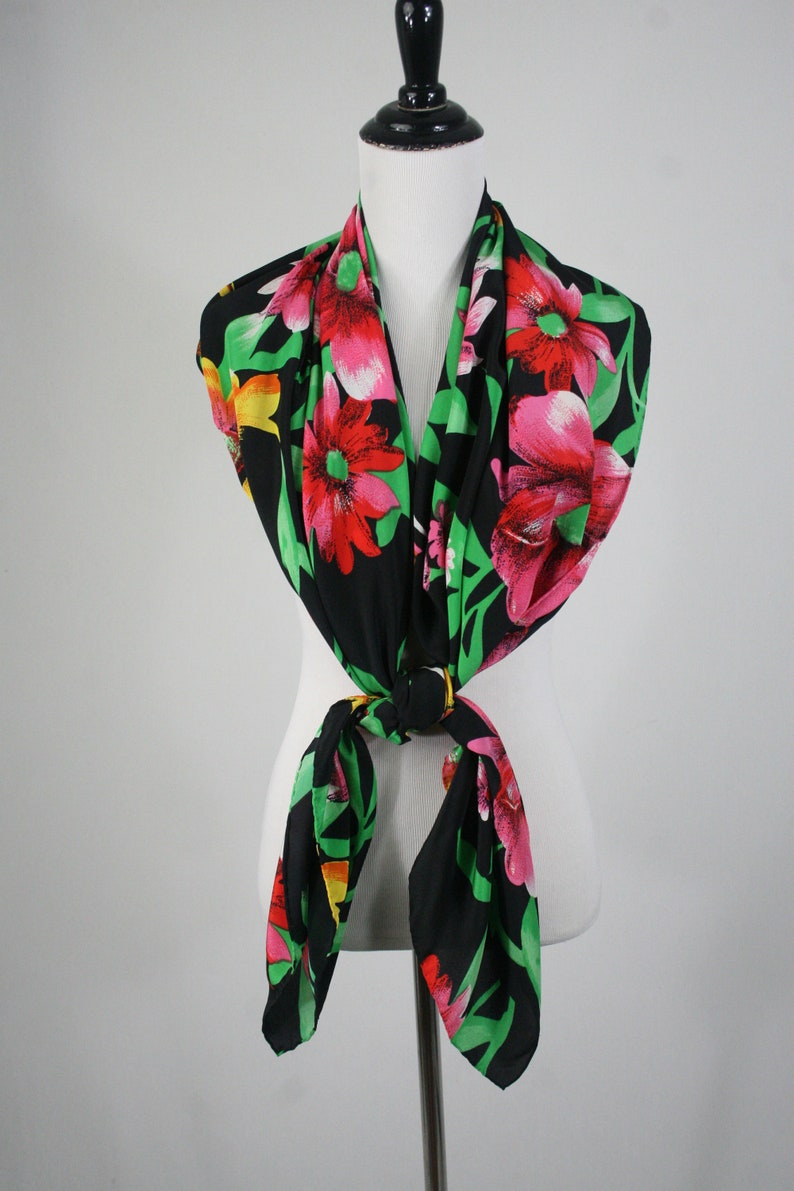 May include: A black silk scarf with a floral print featuring large pink, red, and yellow flowers on a black background. The scarf is tied around a white mannequin's neck.