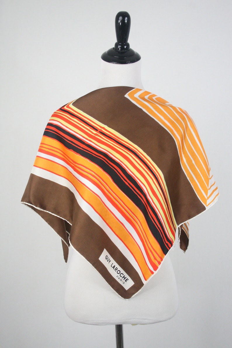 May include: A brown, orange, white, and black striped silk scarf with a white tag that reads 'GUY LAROCHE PARIS'.