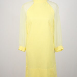 May include: A yellow dress with sheer sleeves. The dress has a high neck and a straight silhouette.