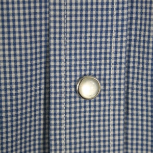 May include: A close-up of a blue and white gingham fabric with a single white button.