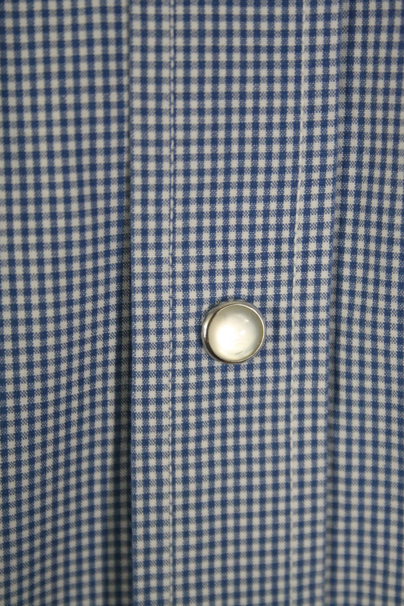May include: A close-up of a blue and white gingham fabric with a single white button.