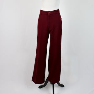 May include: Burgundy-colored, high-waisted pants with a wide-leg design. The pants are displayed on a mannequin against a white backdrop. The pants have a button and zipper closure and pockets.