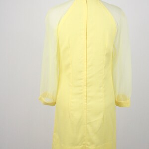May include: A yellow dress with sheer sleeves. The dress has a high neckline and a fitted silhouette.