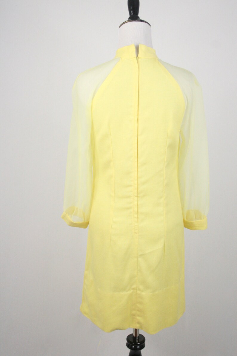 May include: A yellow dress with sheer sleeves. The dress has a high neckline and a fitted silhouette.