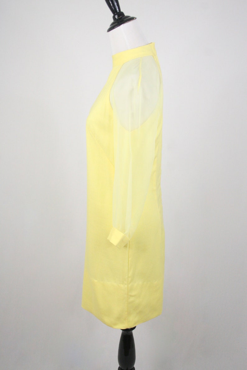 May include: A yellow dress with sheer sleeves. The dress has a high neckline and a fitted silhouette.