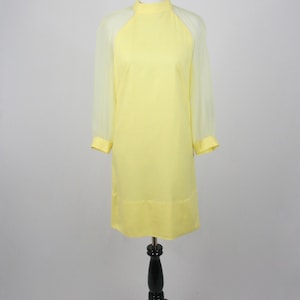 May include: A yellow dress with sheer sleeves. The dress has a high neck and a simple, straight silhouette.