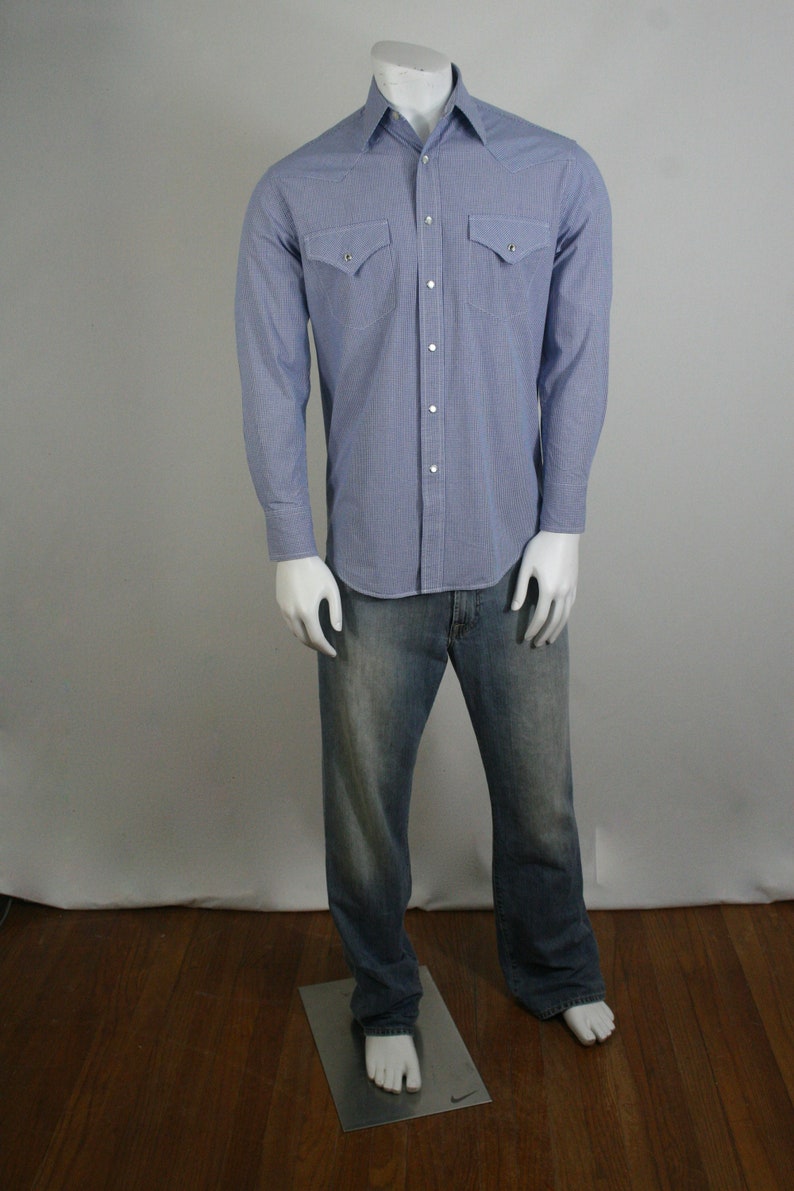 May include: A blue and white checkered long-sleeve shirt with two chest pockets and a button-down collar. The shirt is paired with blue jeans.
