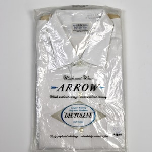 May include: A white Arrow dress shirt, folded and packaged in a clear plastic bag. The shirt has a button-down collar and is labeled "Wash and Wear" with "Dectolene" for soft collar and wrinkle-free wear.